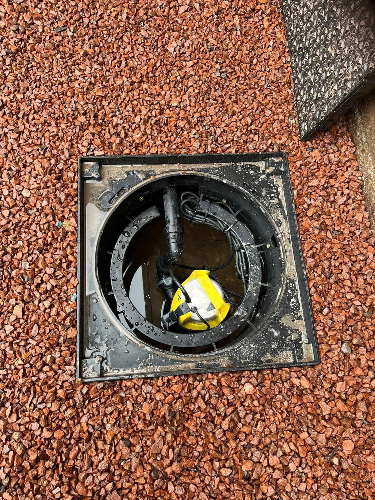 Pump chamber set into red gravel with a submersible pump fitted inside