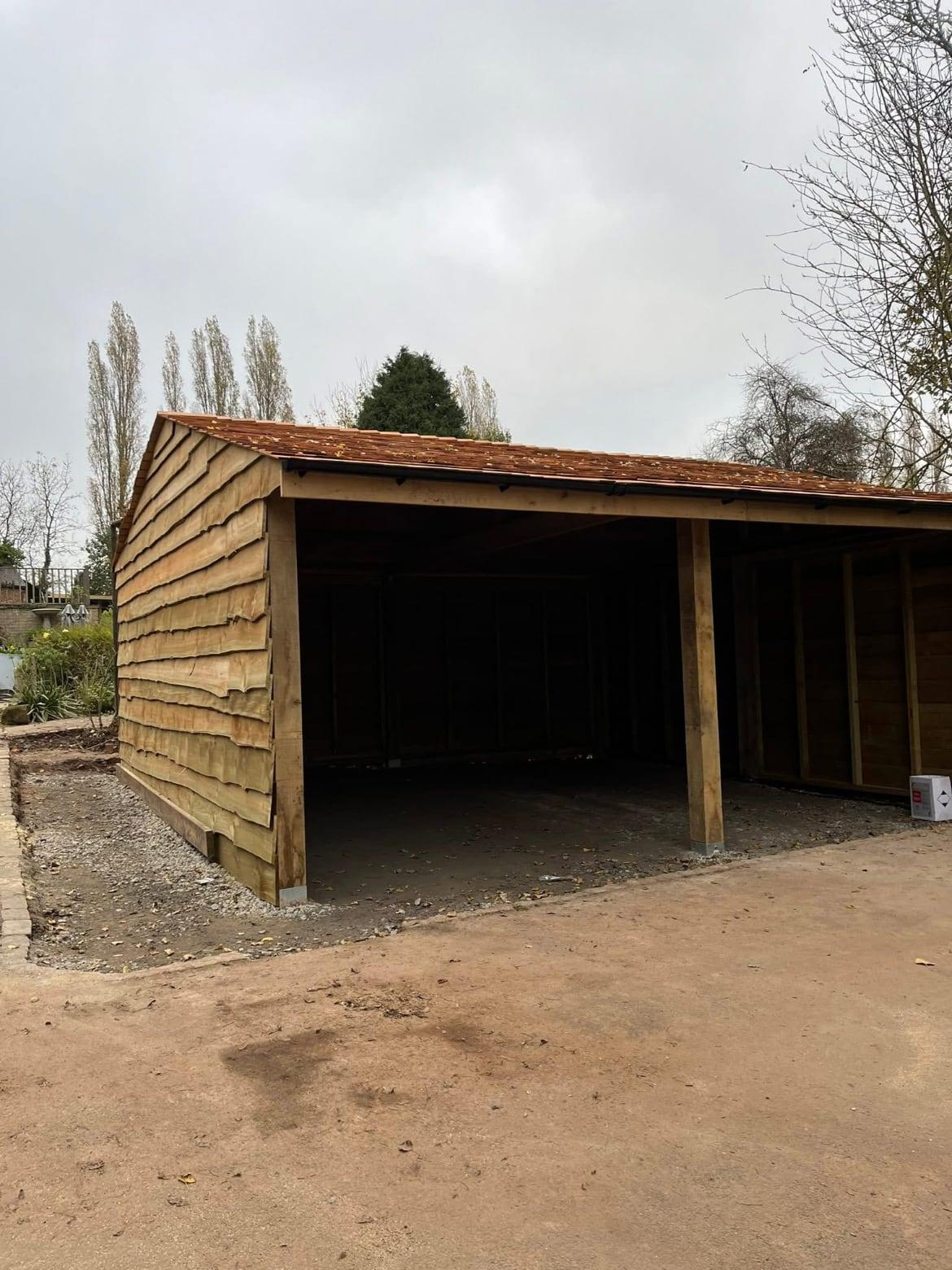 Open-fronted timber garage with two bays, clad in waney-edge boards