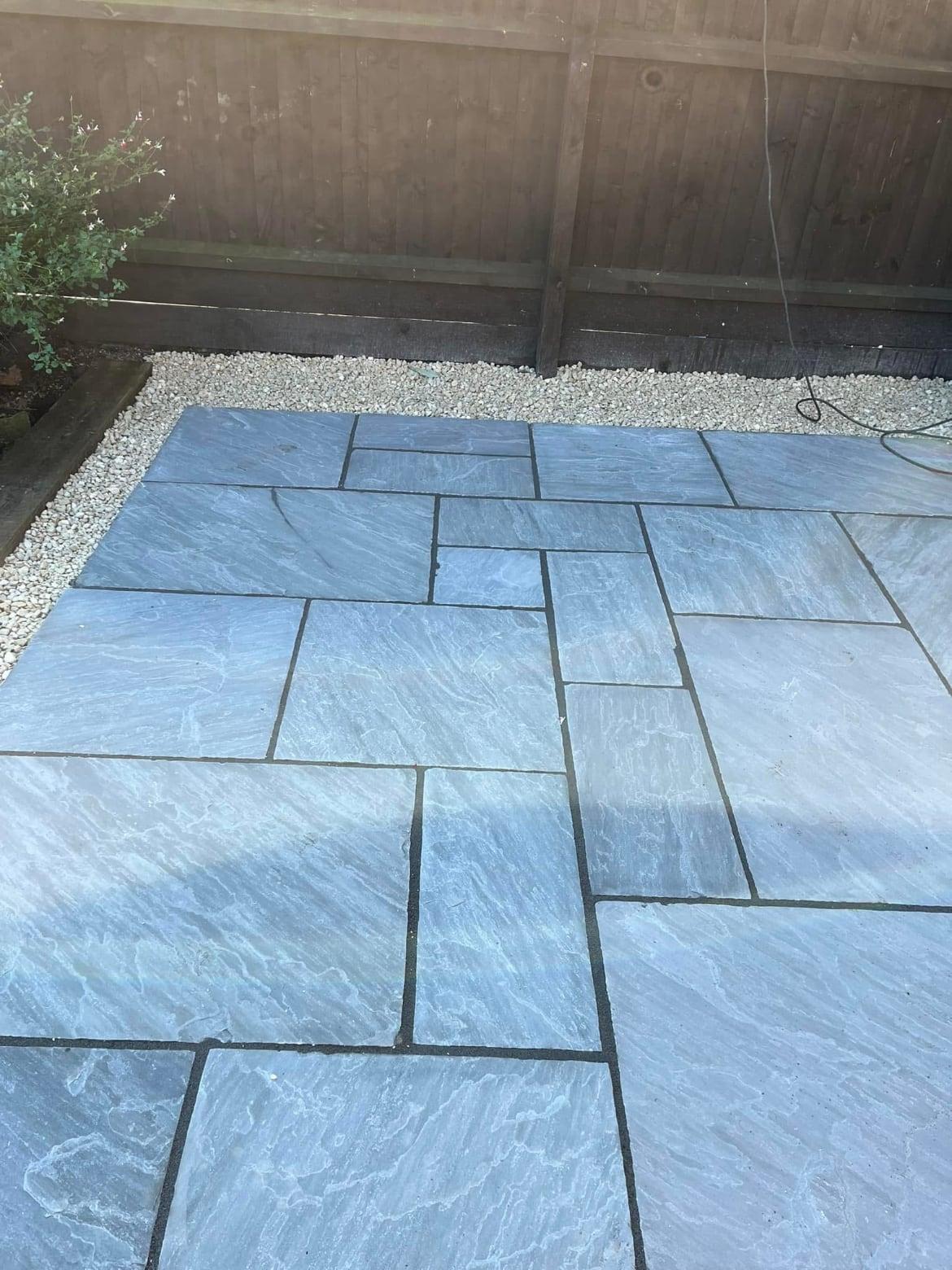 Blue-grey sandstone paving finished with a white gravel border against a timber fence