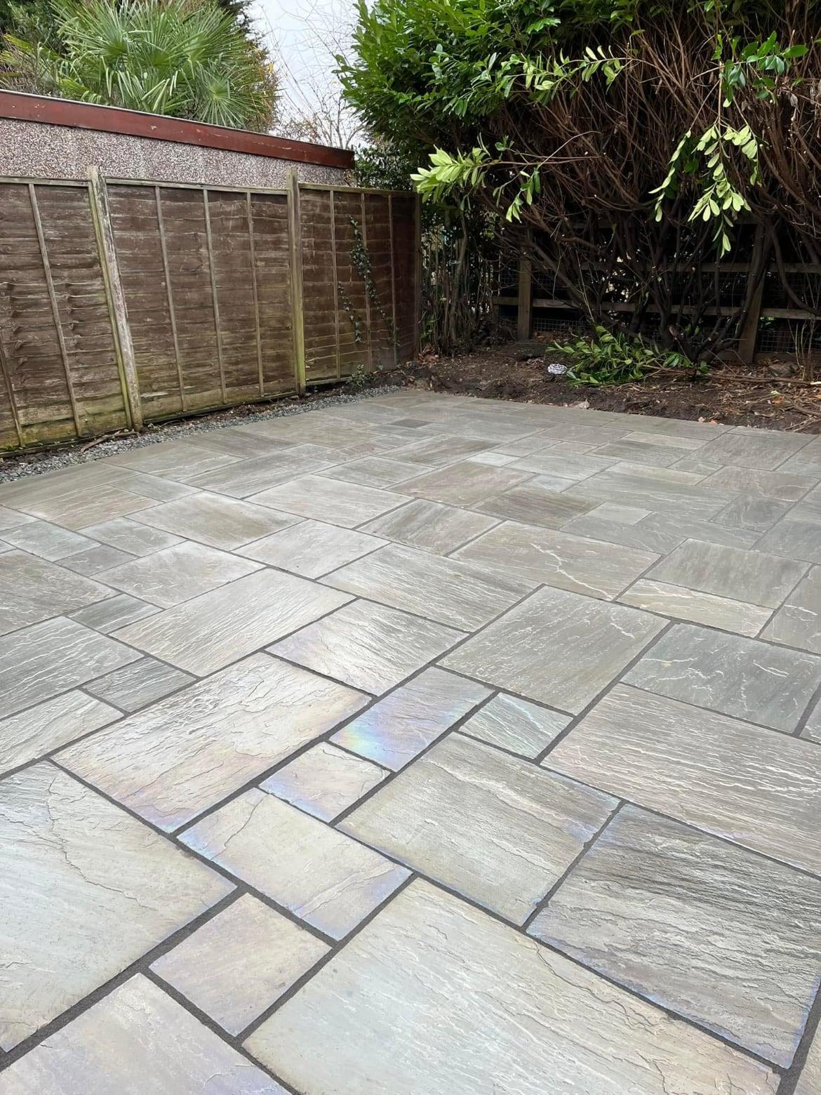 Newly laid sandstone patio in a mature garden with lap panel fencing and established shrubs